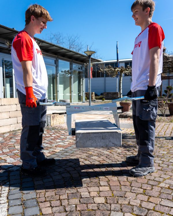 Zwei Bauarbeiter heben einen Betonstein mit einem ergonomischen Greifwerkzeug von Ambros-Technik.